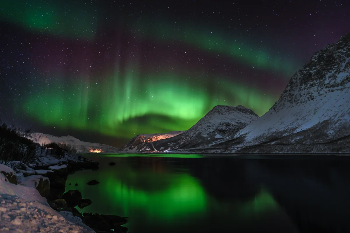 Green northern lights above snow-covered mountains reflected in a still fjord